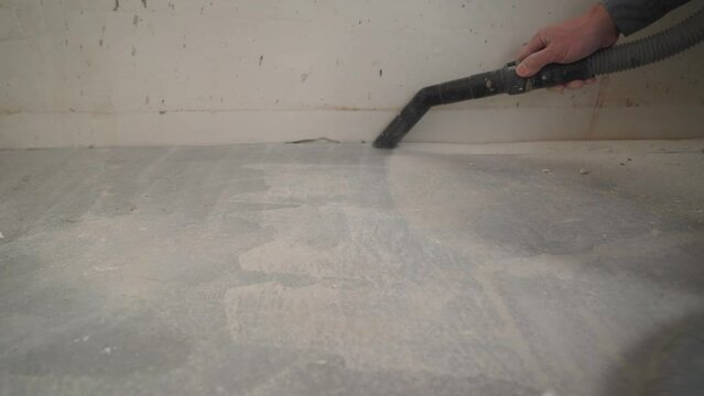Worker washes the floor with a vacuum cleaner from industrial concrete dust and cement mud during home renovation. A worker vacuums a concrete floor.