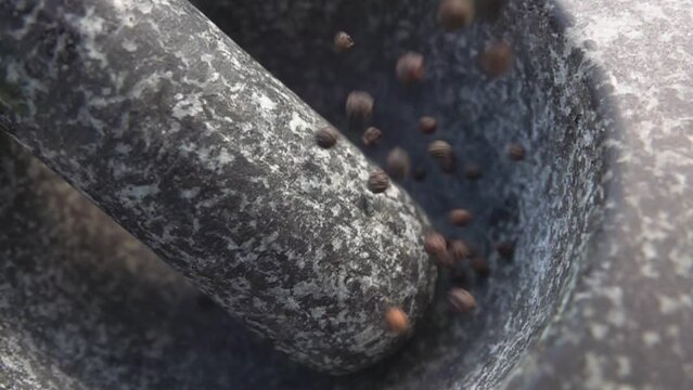 Spicy black peppercorns are falling into the grey stone mortar