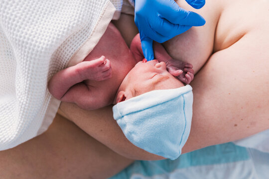 Nurse putting a finger in newborn baby mouth to check his sucking reflex.