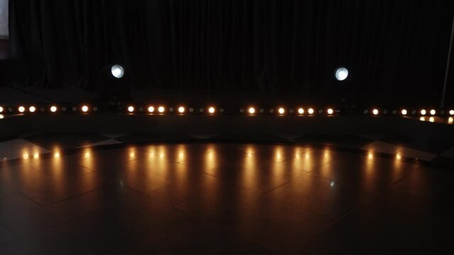 Horizontal row of round warm-colored halogen lights flashing alternately. On tiled floor in dark hall, rays from lanterns are reflected, forming light music.