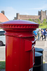 Traditional red post box in Bamburgh village, Northumberland. With out of focus castle in background