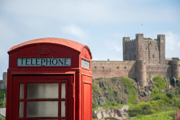 Fototapeta premium Close up of a traditional red UK telephone box in Bamburgh, UK. Out of focus castle in background