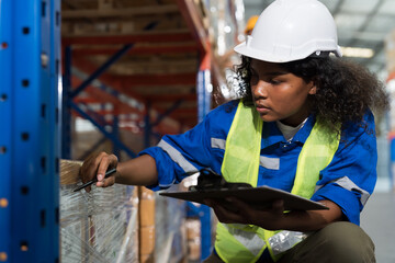 African American female warehouse worker wearing hard hat and uniform checks stock and inventory in the retail warehouse. Woman worker working in the storage warehouse