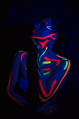 Fashion model woman in neon light, portrait of a beautiful model with fluorescent makeup, body art design in UV, painted face, colorful makeup, on a black background of a girl.