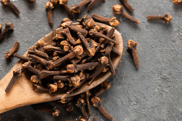 Dry cloves in wooden shovel or spoon on rustic table, fresh herb spice concept 