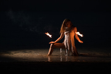Caucasian woman in a white dress juggles with fireballs in the sea. Fire and water at night. Fire...