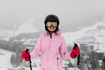 Portrait of preteen girl skier on snowing slope against aerial view of ski resort