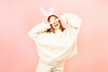 A girl with rabbit ears dances on a pink background. Easter holiday, smile and party. The girl is posing in the studio.