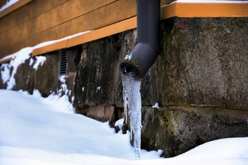 icy drainpipe near the stone foundation of an old house