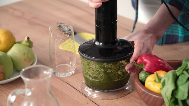young woman monitors her weight and pours a cocktail of chopped vegetables into a glass in an electric blender on the kitchen table, close-up
