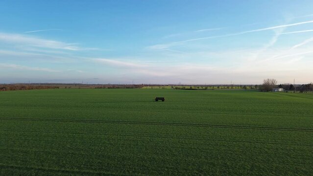 H&auml;nger von einem Traktor steht auf einem gr&uuml;nen Feld mit Spuren, Flug n&auml;her dran mit einer Drohne