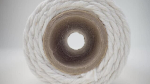 Macro shot spool of hemp rope on white background. Slider dolly extreme close-up roll of thread. Laowa 24mm lens camera glides inside reel of thick white thread, flight through round object