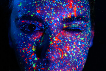 Beautiful young sexy girl dances with paint on television. Girl with neon body art in colored light.