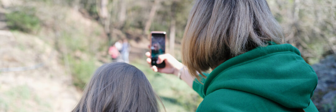 Mom and daughter sit with backs and take pictures of nature on smartphone