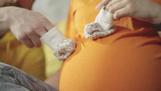 Happy pregnant couple in love resting and having fun at home. Father and mother are expecting a child. A man and a woman play on a big belly with baby socks.