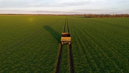 Hänger von einem Traktor steht auf einem grünen Feld mit Spuren, Symmetrisch von oben mit blauen Himmel