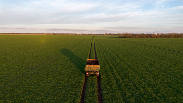 H&auml;nger von einem Traktor steht auf einem gr&uuml;nen Feld mit Spuren, Symmetrisch von oben und tiefer Sonne