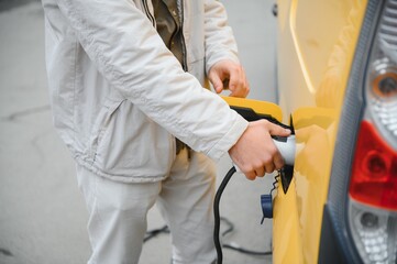 Man Holding Power Charging Cable For Electric Car In Outdoor Car Park. And he s going to connect the car to the charging station in the parking lot near the shopping center