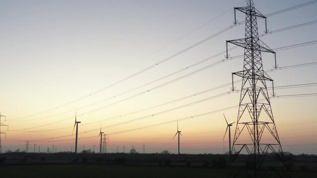 Aerial drone view of wind turbines and pylon for green energy. Sunset concept for climate change initiative with technology England Manchester UK 4K
