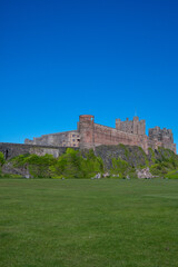 Fototapeta na wymiar View of Bamburgh Castle from the local cricket pitch, against a bright blue summer sky. Northumberland, UK