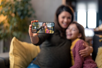 Beautiful cheerful woman and young daughter out of focus smiling looking at phone camera, recording...