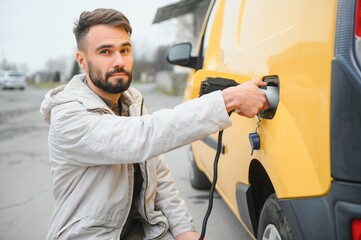 Portrait of a young man standing with charging cable near the charging station