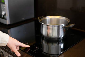 Girl cooking. Girl turning on the hob to heat the water in the pot
