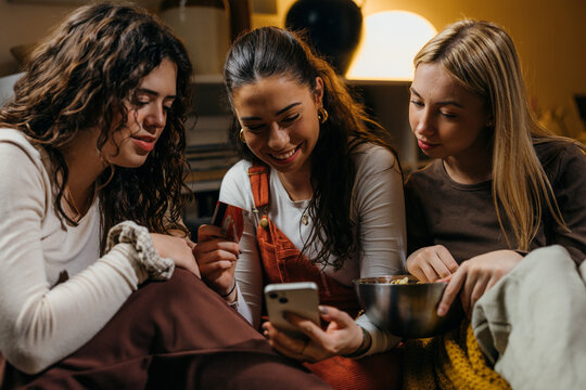 Front view of a three woman using a phone and a credit card to shop online