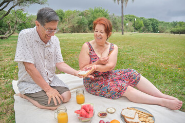 A happy latin senior couple having a picnic breakfast with whole grain bread and crackers, orange...