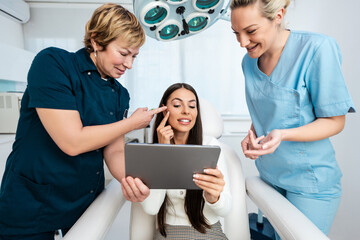 Obraz premium Beautiful and happy brunette woman at beauty medical clinic. She is sitting and talking with two female doctors about face aesthetic treatment.