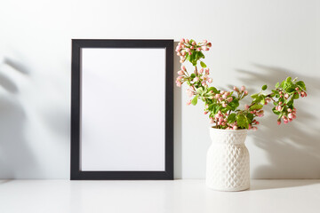 Mockup with a black frame and spring flowers in a vase on a light background. Empty poster frame mockup for presentation design, text, lettering
