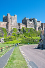 Fototapeta na wymiar View of Bamburgh Castle from the road, against a bright blue summer sky. Northumberland, UK. Platinum Jubilee bunting on nearby fence. Summer 2022