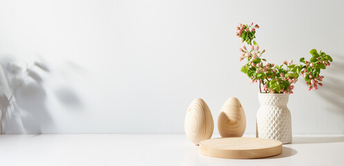 Empty round wooden podium for product presentation. Spring flowers in a vase and easter eggs on a light background.