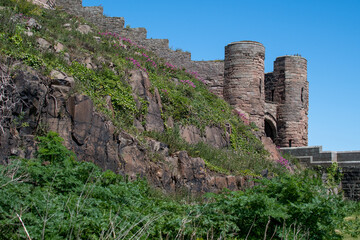 Bamburgh Castle walls and rocky crag against a bright blue summer sky. Northumberland, UK	