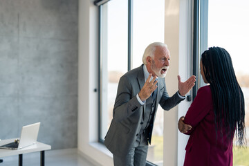 Angry senior businessman company manager yelling at burnout businesswoman putting her under...