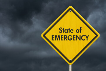 State of Emergency message on warning road sign with stormy sky