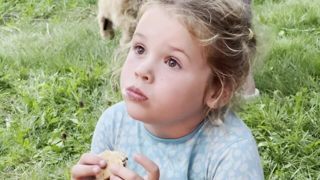 Young girl in blue dress eats a s'more by a campfire