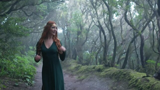 Beautiful woman in an elf costume is walking in a magic green enchanted forest.
