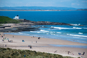 A busy summer's day on Bamburgh beach, Northumberland, with people on beach. Bamburgh lighthouse in distance