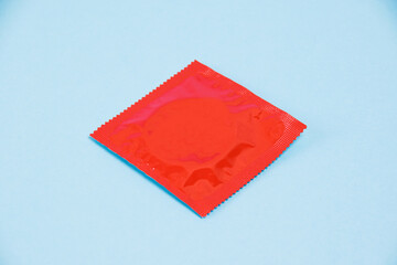 Condom in red package on blue paper background with copy space