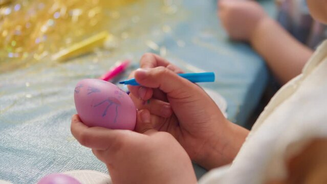 Cute little children coloring Easter eggs with their grandparents sitting at the table in the kitchen hands of a girl painting an egg. Close-up of a girl's hands holding an Easter egg and coloring it.
