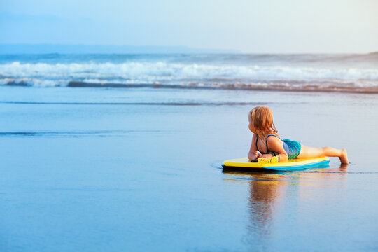 Little baby girl - young surfer with bodyboard has fun on sea beach. Family lifestyle, people outdoor water sport lessons and swimming activity on summer vacation with child in adventure surf camp.