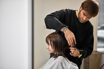 Professional male hairdresser cutting female hair in salon