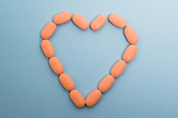 Pink pills laid out on a paper background in the shape of a heart, flatlay. Concept of prevention and treatment of heart diseases