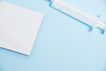 A condom in a package and a syringe on a soft blue background. Concept of protection against...