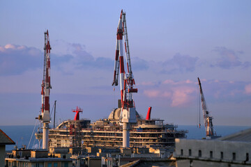 Cranes and cruise ship in the Genoa shipyards site of Sestri Ponente. View from above between the houses of the town at sunset. Genoa, Italy