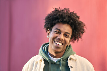 Close up portrait photo of young happy African American cool hipster teen guy face laughing on red city wall lit with sunlight. Smiling cool rebel gen z teenager model standing outdoors. Headshot. - obrazy, fototapety, plakaty