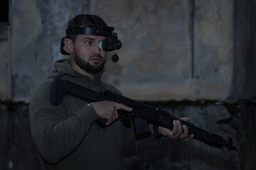 A man with a night vision device and an assault rifle in a war at night.