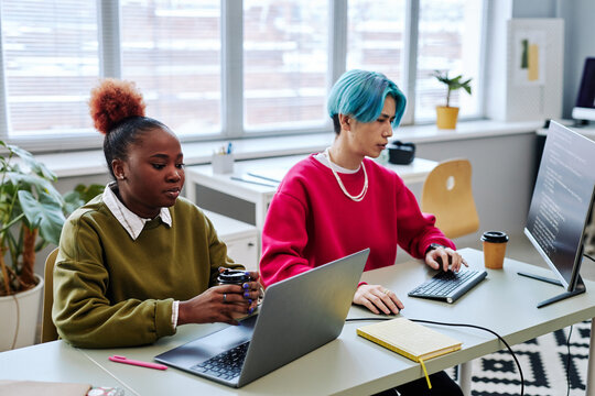 Portrait of two gen Z young people using computers while developing software and writing code in modern office, magenta accent