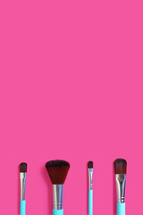 A set of four makeup brushes on a pink vertical background. Four blue makeup brushes in different shapes and sizes. Fashionable women's cosmetics to create facial beauty. Free space for text